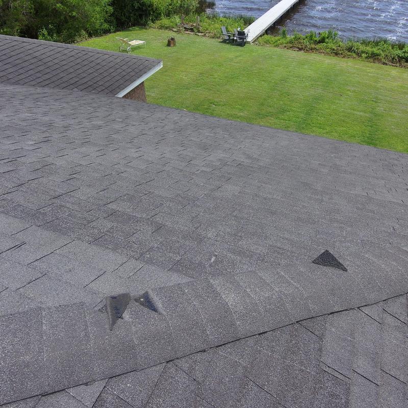 Asphalt roof shingles with wind damage and missing pieces Asphalt roof shingles with wind damage and missing pieces