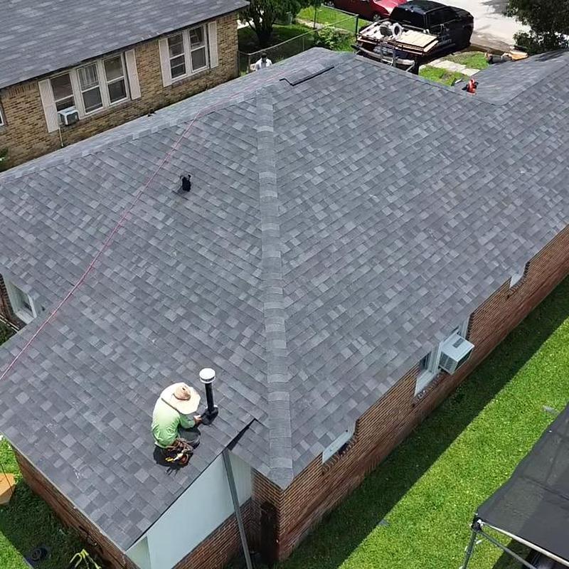 Asphalt shingle roof replacement with worker on chimney pipe