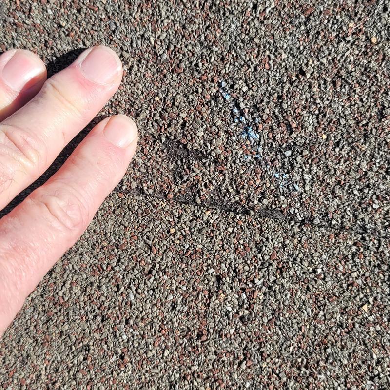 Roof shingles with hail damage close-up and hand for scale