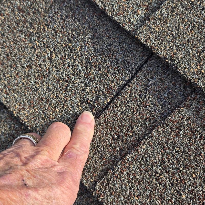Asphalt shingle roof hail damage close-up with finger pointing