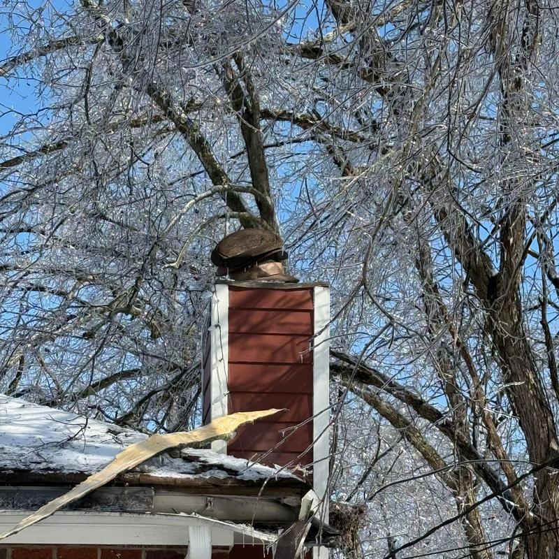 Chimney repair with ice-covered trees and roof damage
