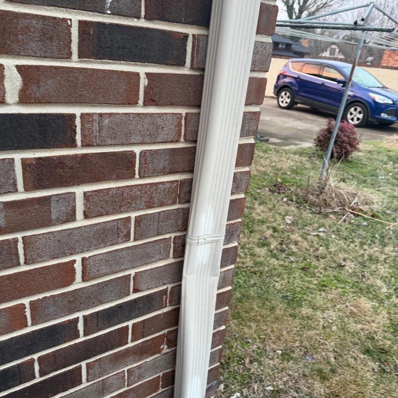 Downspout dent on brick wall exterior near lawn