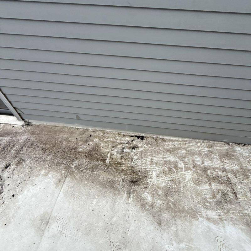Concrete patio surface with dirt and staining near siding