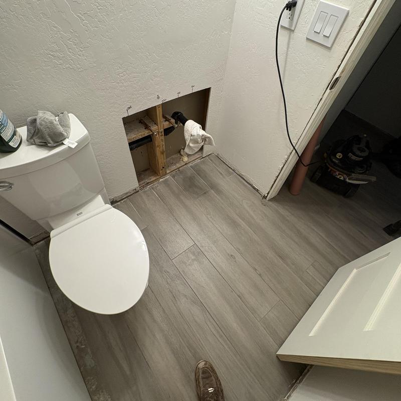 Toilet installation area with exposed drain pipe and tiled floor