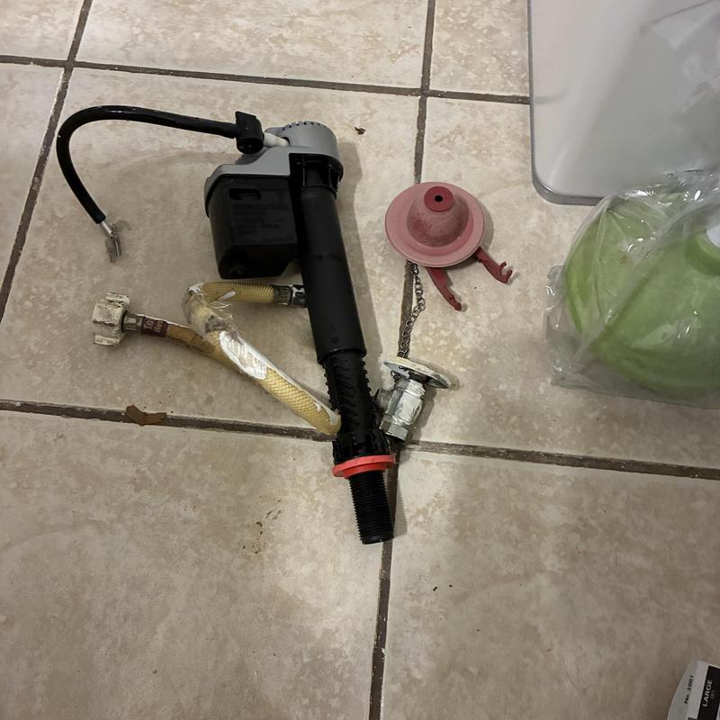 Toilet fill valve and flapper replacement parts on tile floor Toilet fill valve and flapper replacement parts on tile floor
