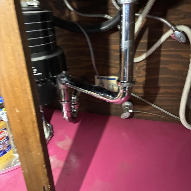 Chrome kitchen sink P-trap and drain pipes under cabinet