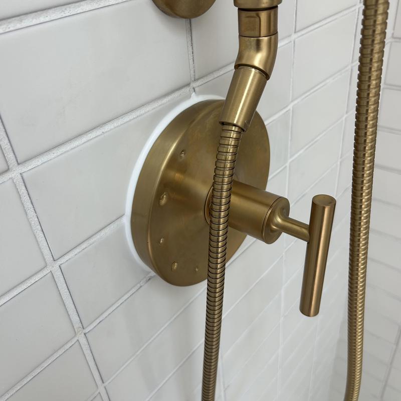 Shower valve and hose with gold finish on white tile
