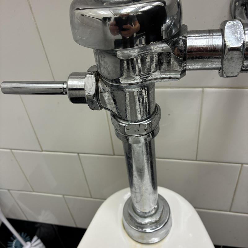 Flush valve on men's toilet in restaurant restroom Flush valve on men's toilet in restaurant restroom