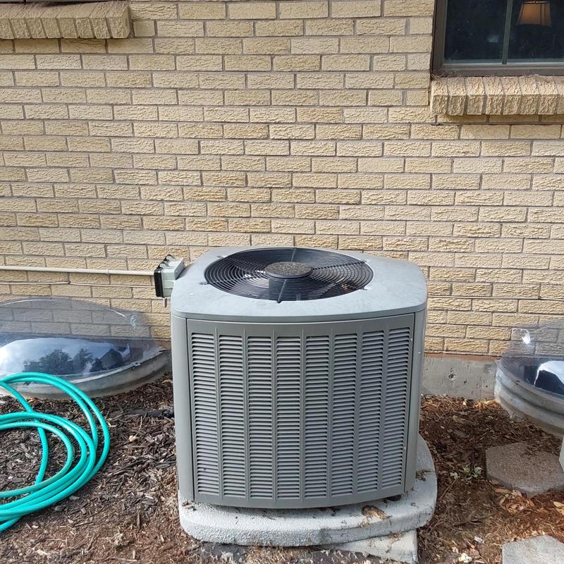 Air conditioner unit outside brick house with garden hose