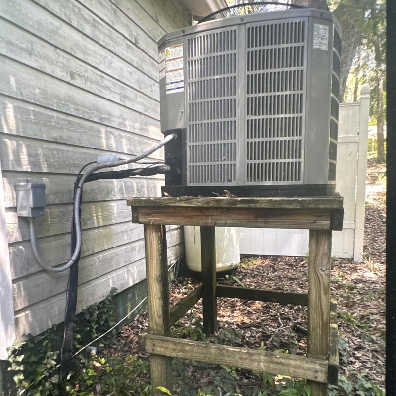 Air conditioner outdoor unit on wooden stand in yard