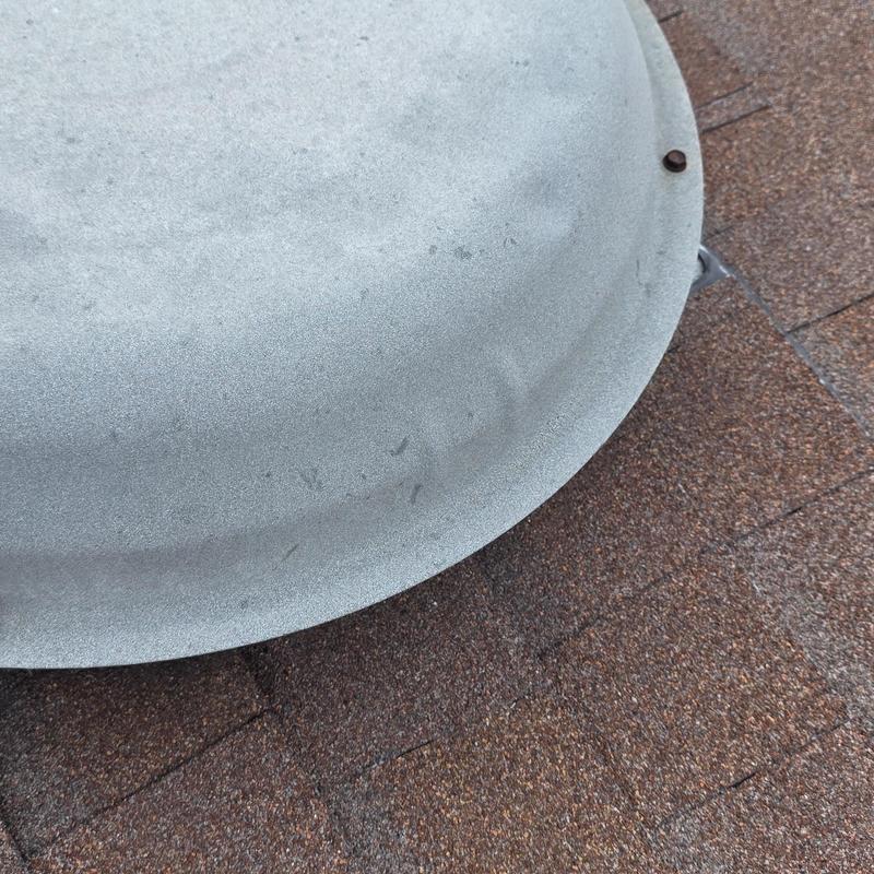 Metal roof vent with hail damage dents on shingles
