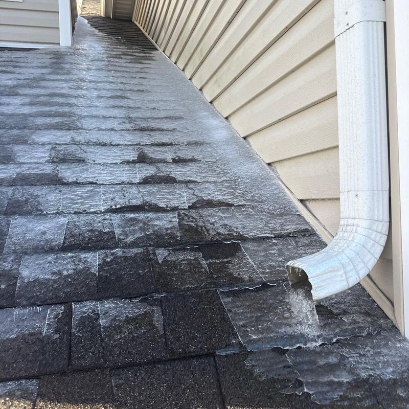 Asphalt shingle roof with ice buildup near downspout