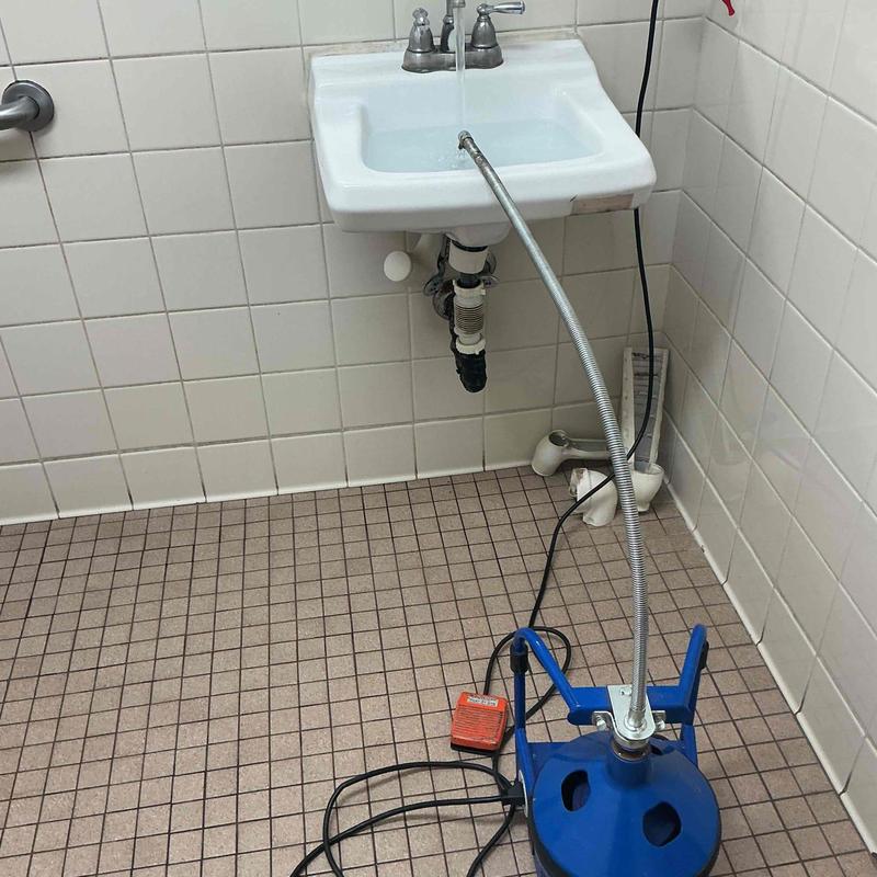 Drain line snaking machine by wall-mounted sink