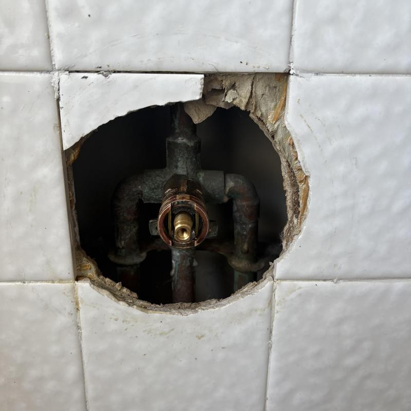 Shower valve cartridge exposed behind tile wall