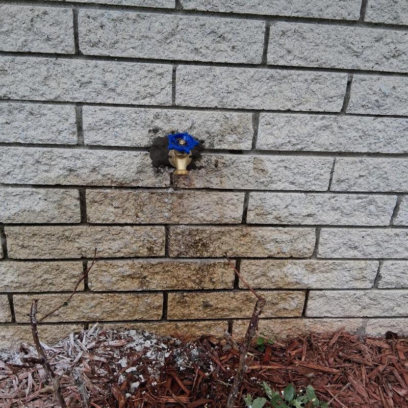 Outdoor silcock valve with new blue handle on brick wall