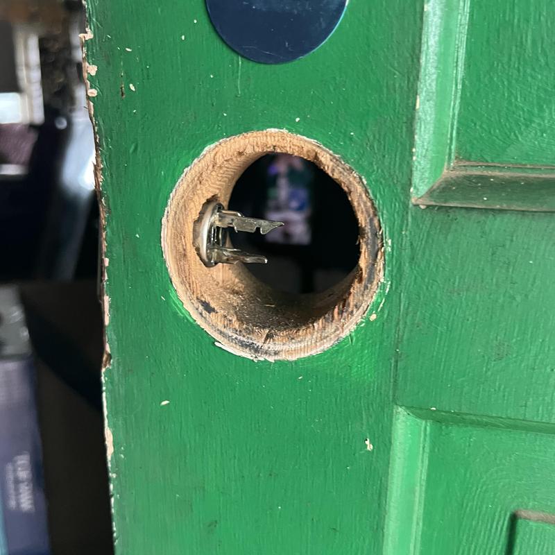 Door latch hole in green wooden door without knob