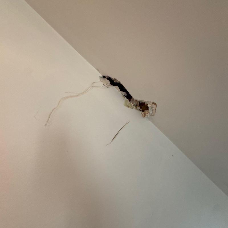 Drywall corner hole with exposed lath and cracks