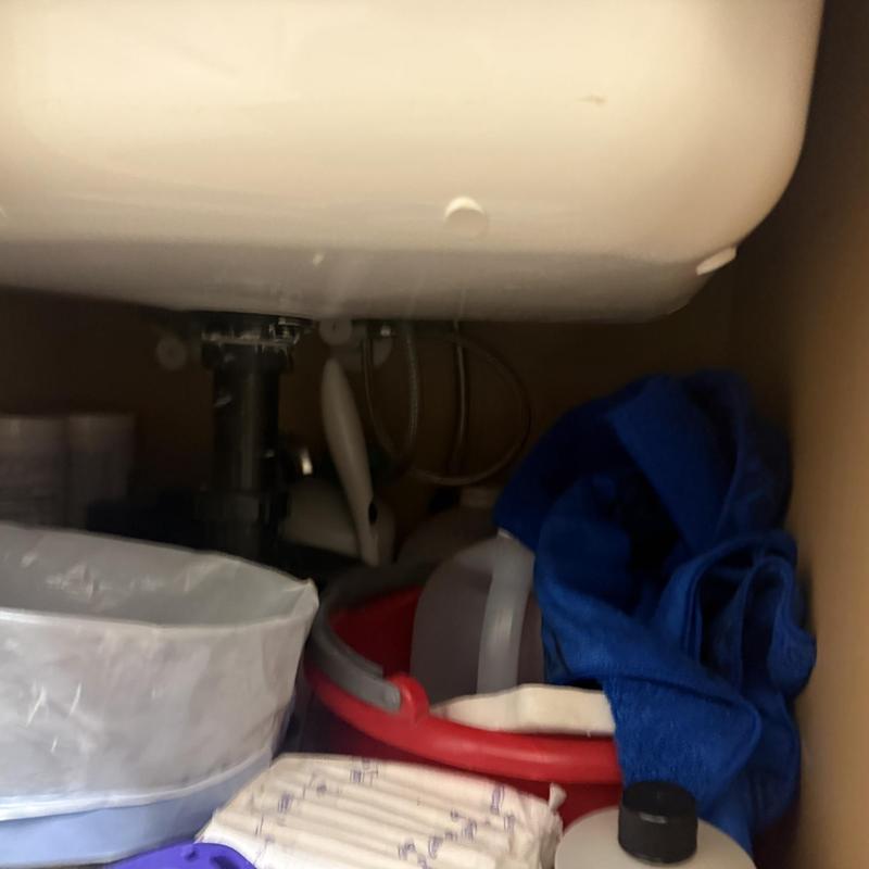 Kitchen sink plumbing with cleaning supplies and cloths