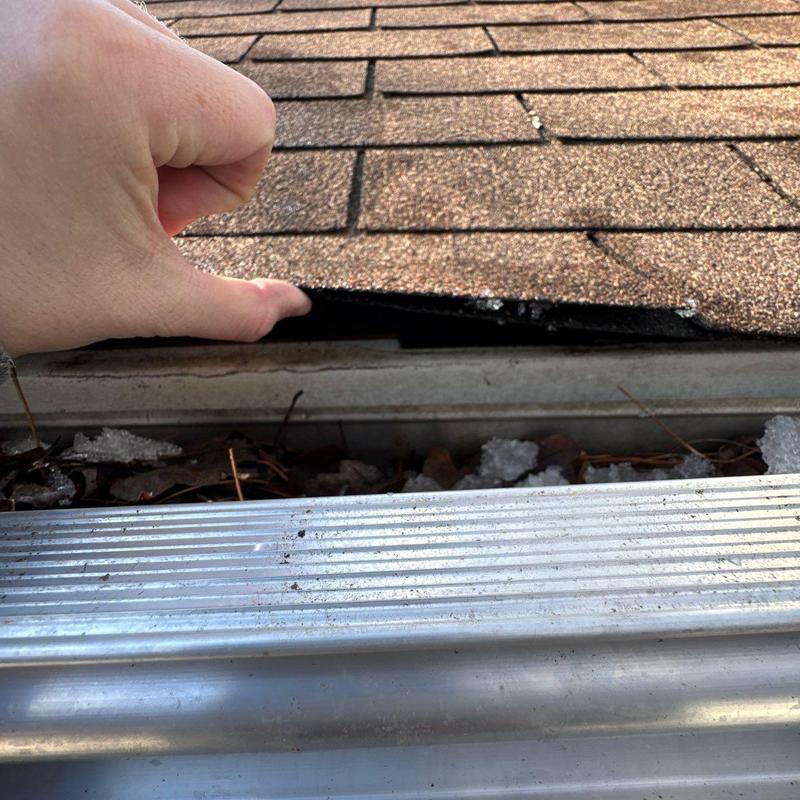 Roof shingles lifted to show hail damage and debris in gutter
