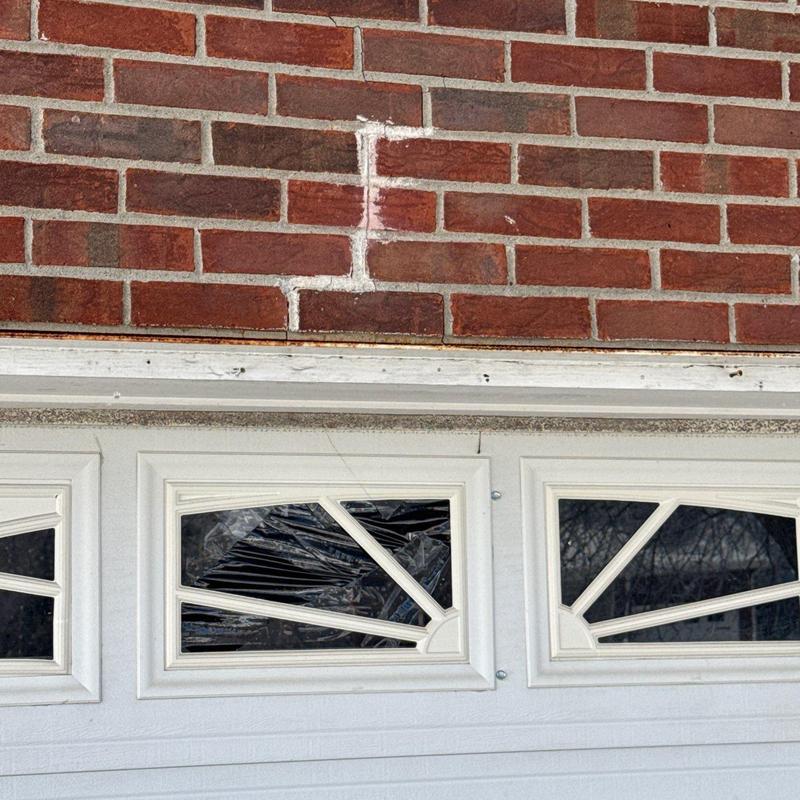 Garage door window with cracked glass and brick wall above