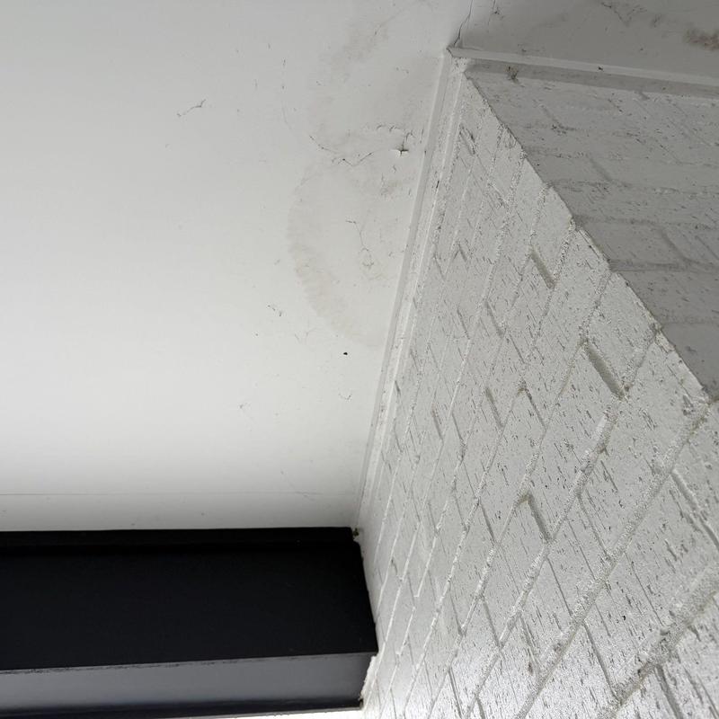 Ceiling water stain and cracked paint near brick wall