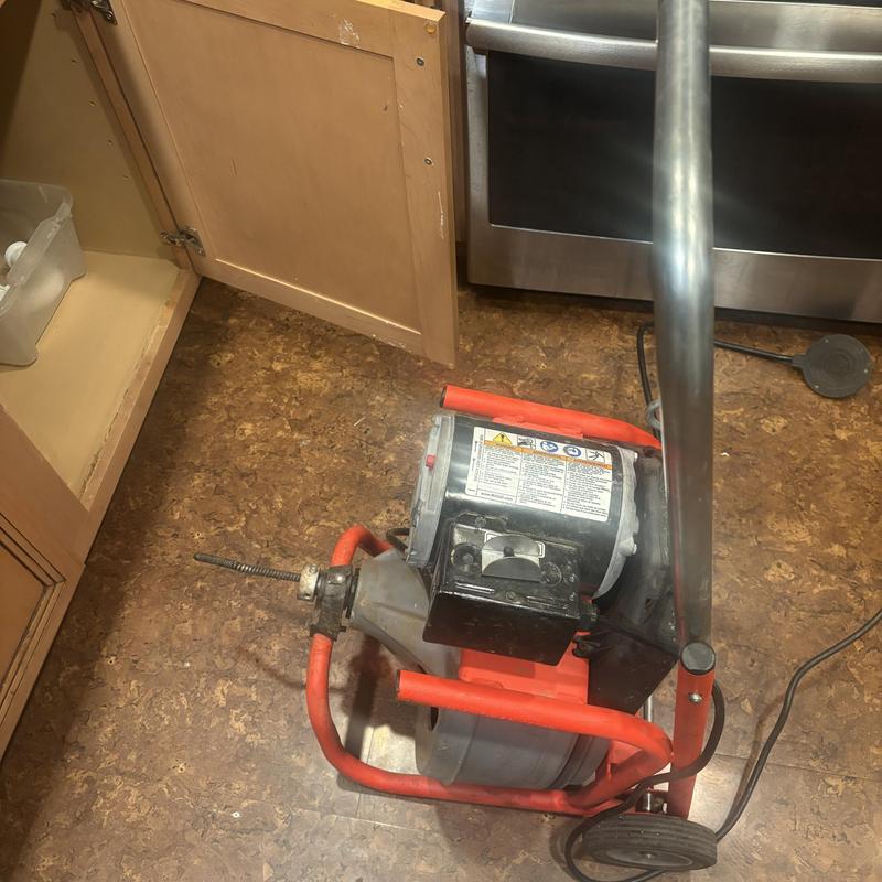 Drain snake machine clearing kitchen drain line in cabinet