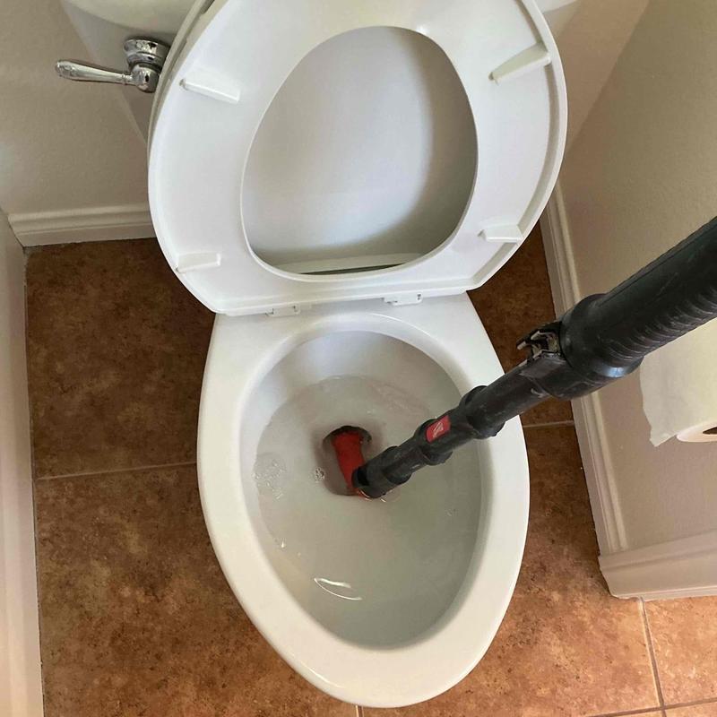 Toilet drain auger clearing clog in bathroom toilet bowl