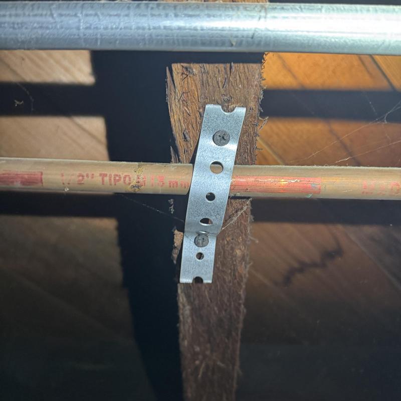 Copper water line secured with metal pipe strap