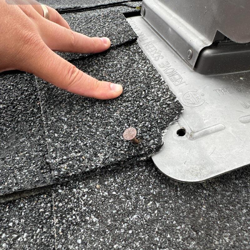 Asphalt roof shingles lifted by hand near metal flashing