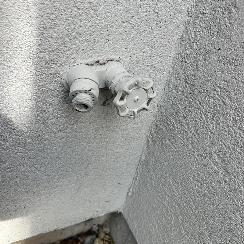 Hose bib exterior wall plumbing connection, white textured wall