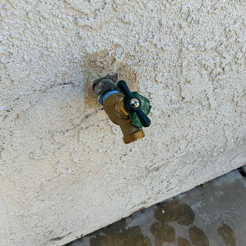 Hose bib with green handle on textured wall