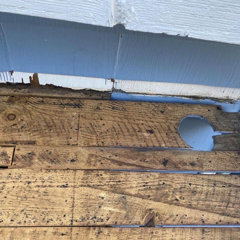 Wood subfloor with cut hole near wall baseboard