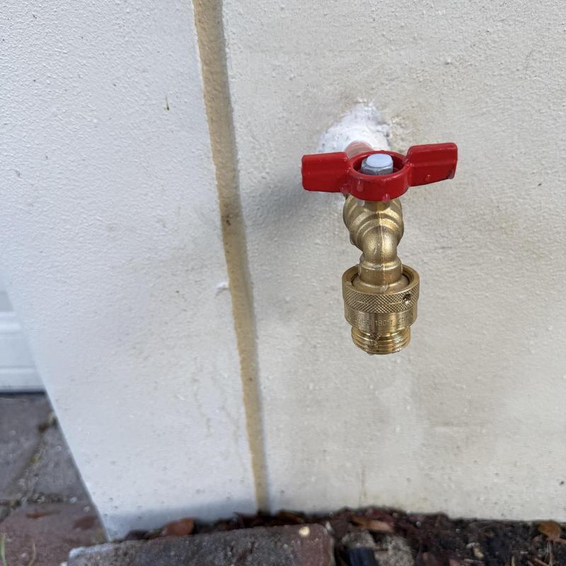 Outdoor hose bib with red handle on house wall
