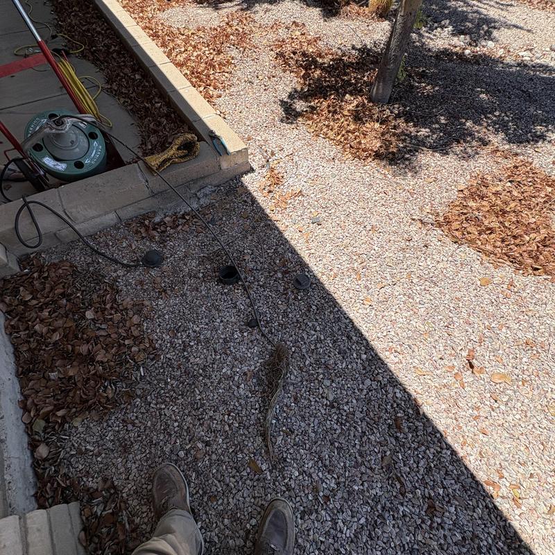 Outdoor drain snake cleaning with debris removal in gravel area