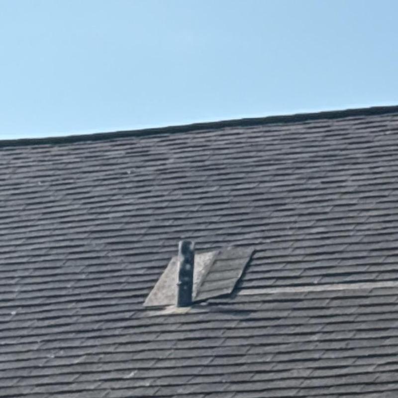 Plumbing pipe boot on shingled roof under clear sky