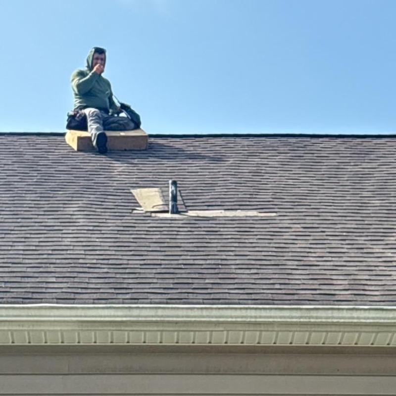 Plumbing pipe boot area on shingled roof with worker sitting