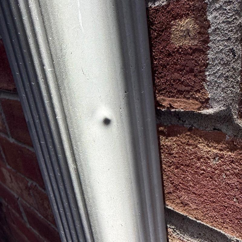 Metal downspout with hail dent and brick wall background