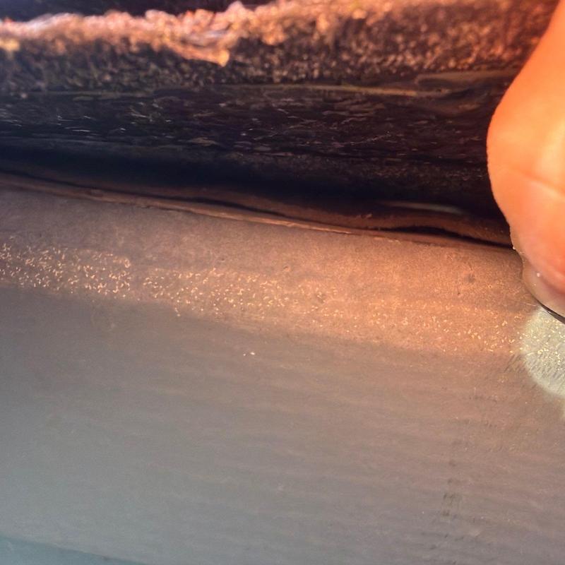 Roof shingle underlayer lifted by hand showing gap