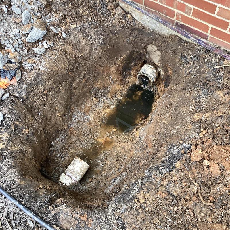 Sewer line excavation with exposed pipe near building wall
