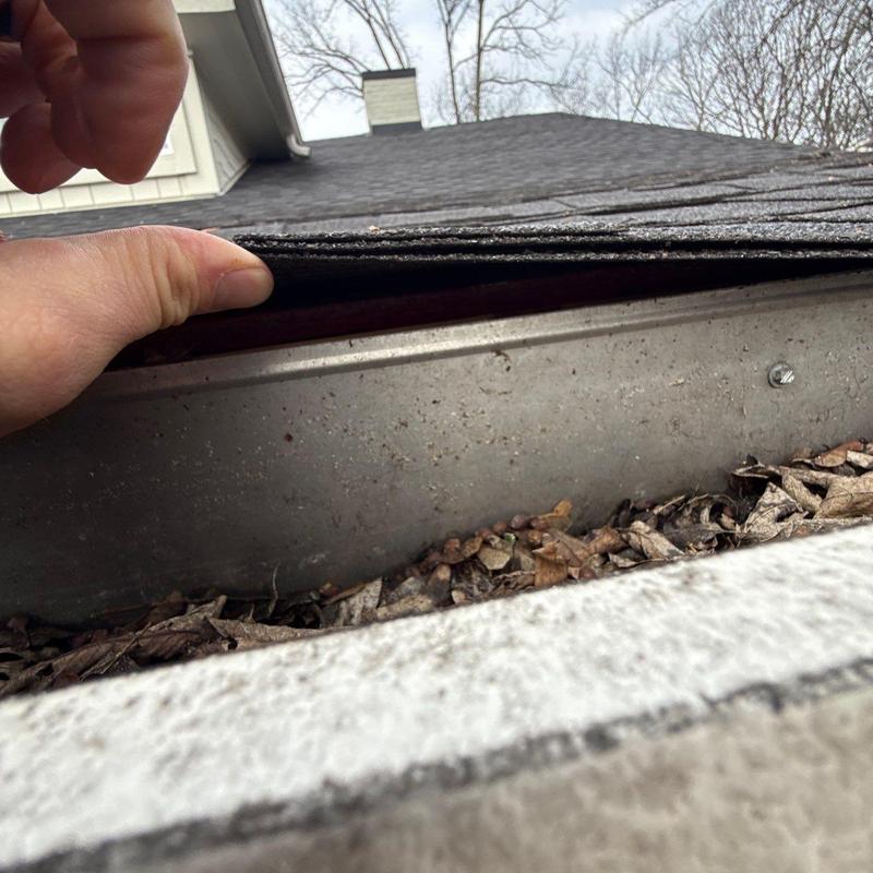 Roofing shingles lifted to inspect gutter debris buildup
