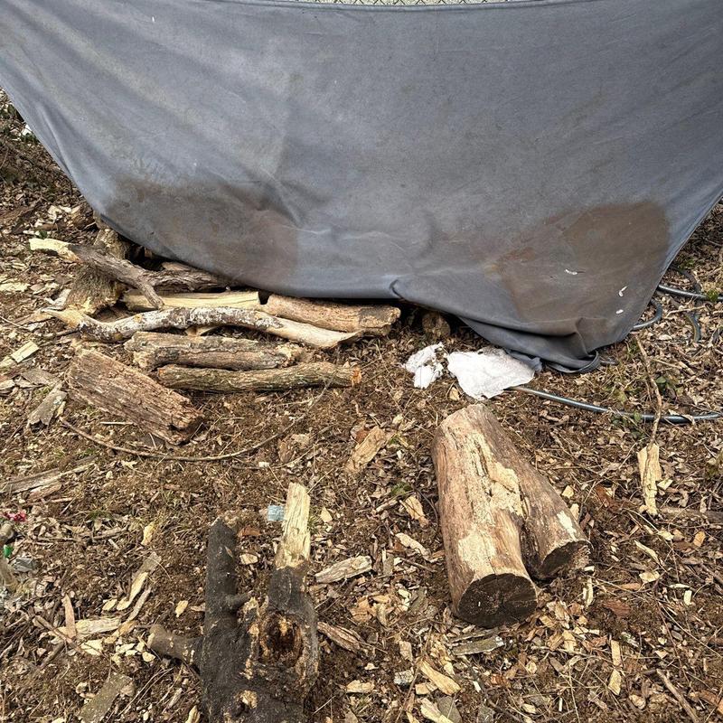 Firewood pile covered with tarp on dirt ground
