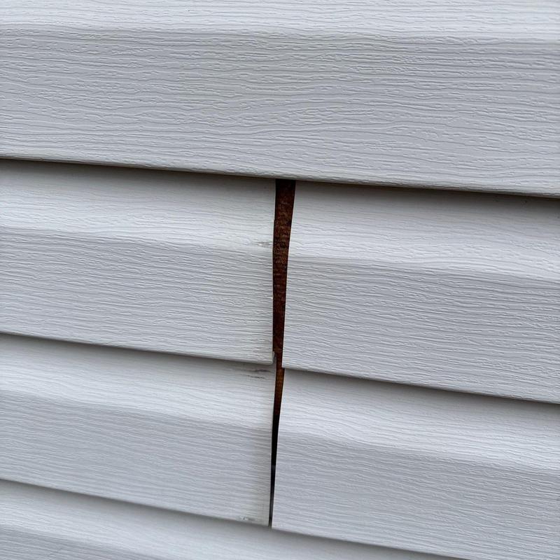 Vinyl siding gap with visible backing wood damage