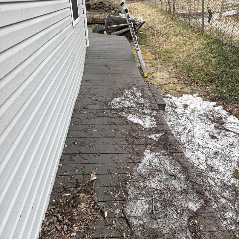 Wooden deck with debris and patches of snow near house siding