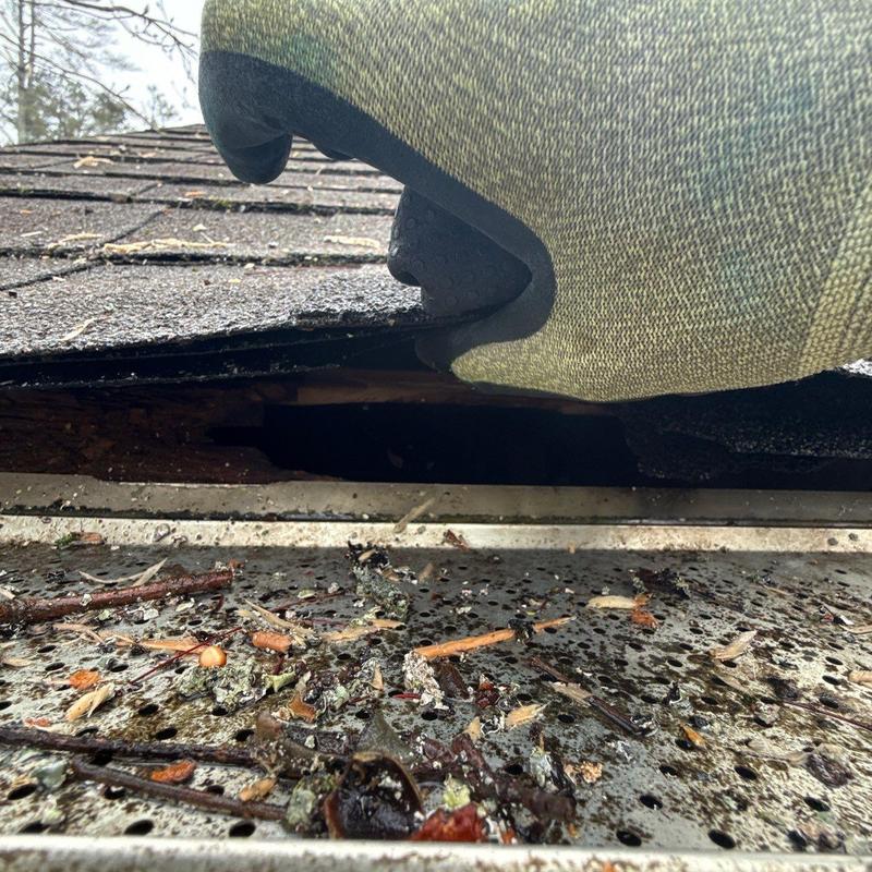 Roof shingles lifted showing damage above gutter debris