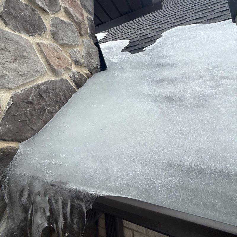 Roof shingles with heavy ice buildup near stone chimney
