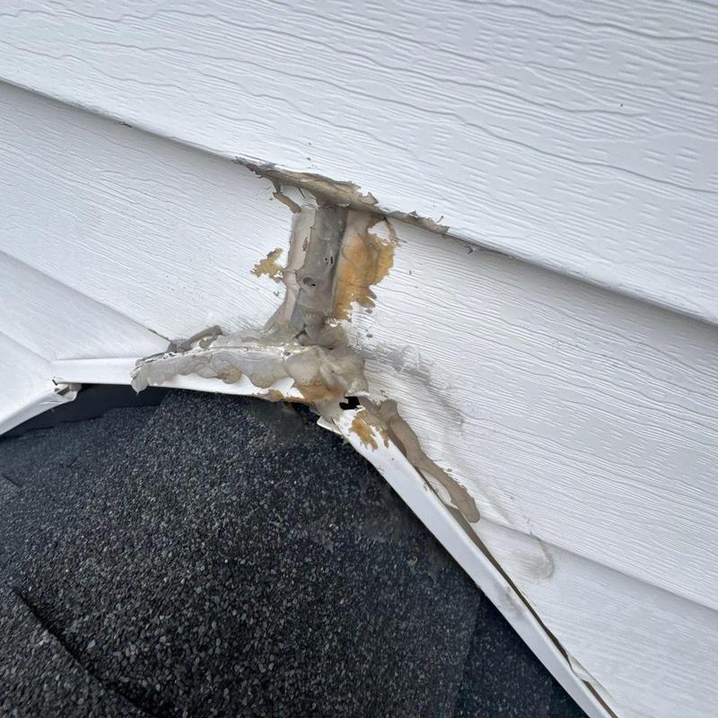 Vinyl siding damage with sealant and flashing on roof edge