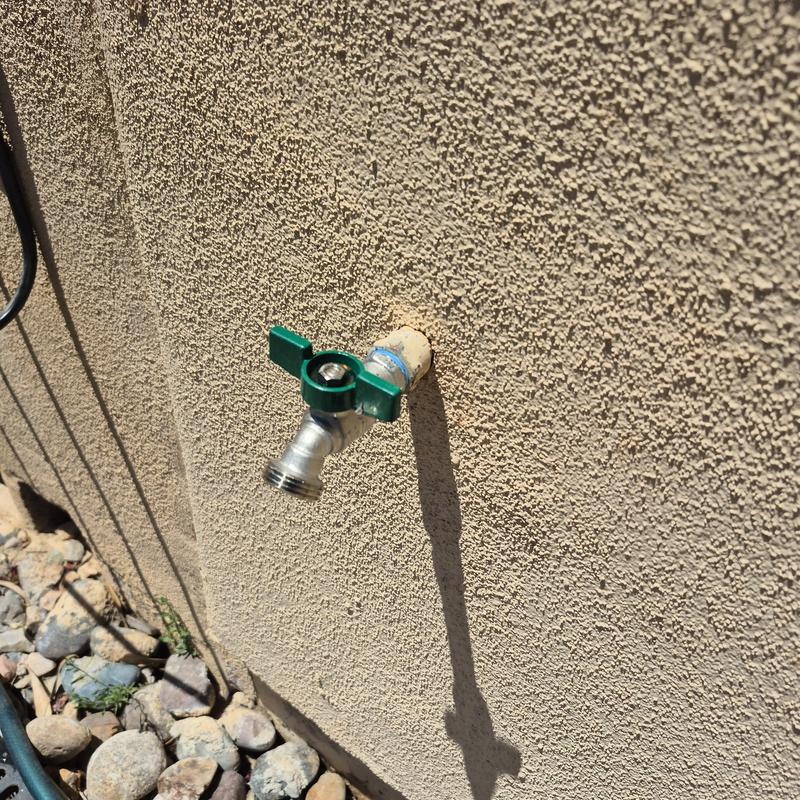 Hose bib with green quarter turn valve on stucco wall