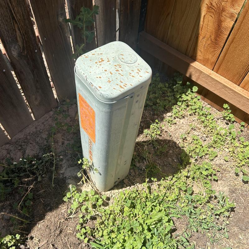 Metal communication utility pedestal by wooden fence Metal communication utility pedestal by wooden fence
