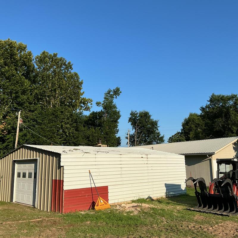 Metal storage shed with debris on roof and tractor nearby Metal storage shed with debris on roof and tractor nearby