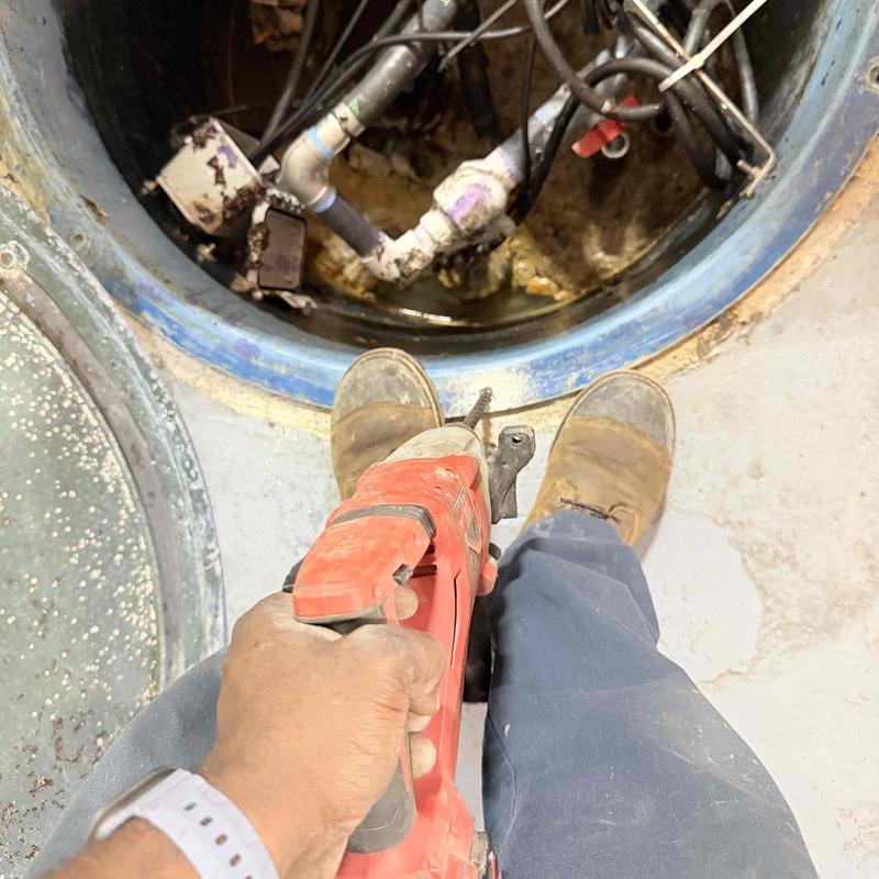 Pump system inside sump pit with power tool in hand Pump system inside sump pit with power tool in hand
